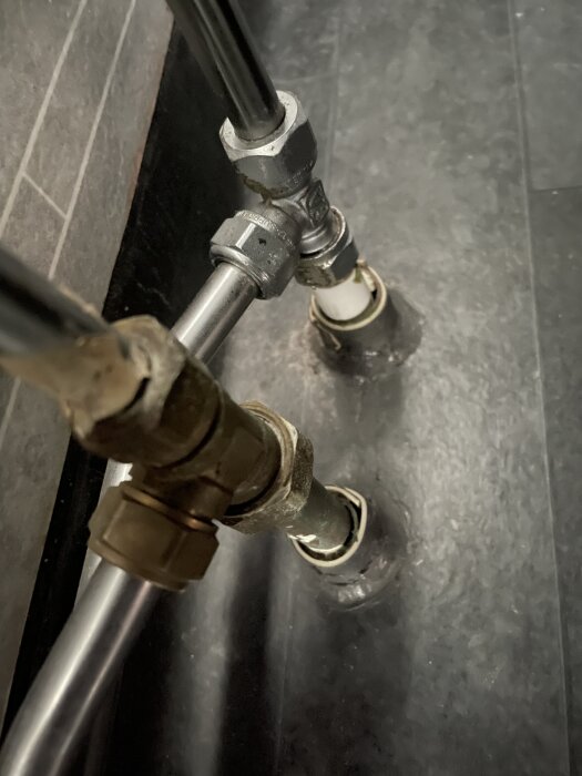 Metallrör och kopplingar genom golv i badrum, omgjort 2020.