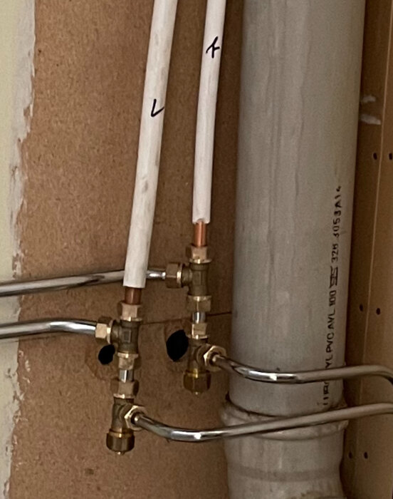 Rörkopplingar och ventiler med märkta rör, del av ett VVS-system. Bakgrund av träpanel, fokus på installationsdetaljer.