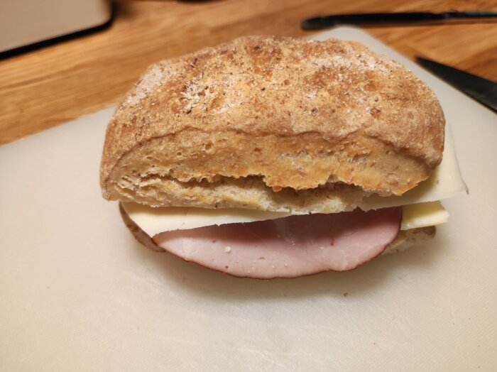 En nybakad fralla med ost och skinka, liggande på en skärbräda.