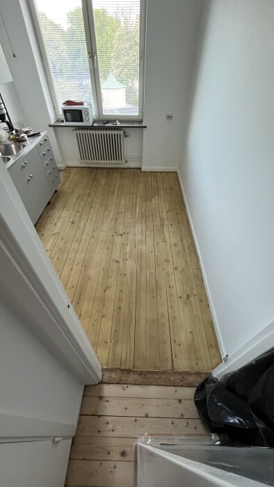 Köket har ett nyligen slipat furugolv med grön nyans, synligt i naturligt ljus från fönstret.