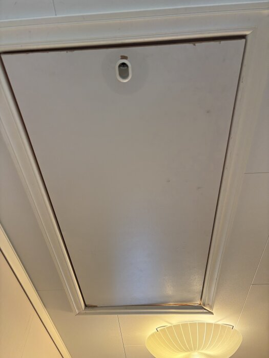 Vit vindslucka i taket med en rund lampa nedanför.