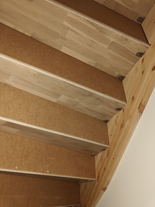 Trätrappa sedd underifrån med mdf-sättsteg fästa med skruvar. Stegen är täckta med latex.