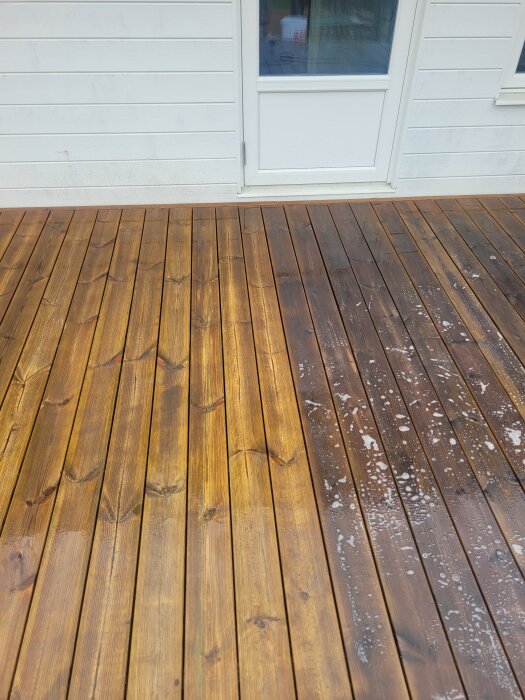 Nyss skurat trädeck, tydlig skillnad mellan rengjord del och smutsig del med mörkare trä och tvålrester på den smutsiga delen.