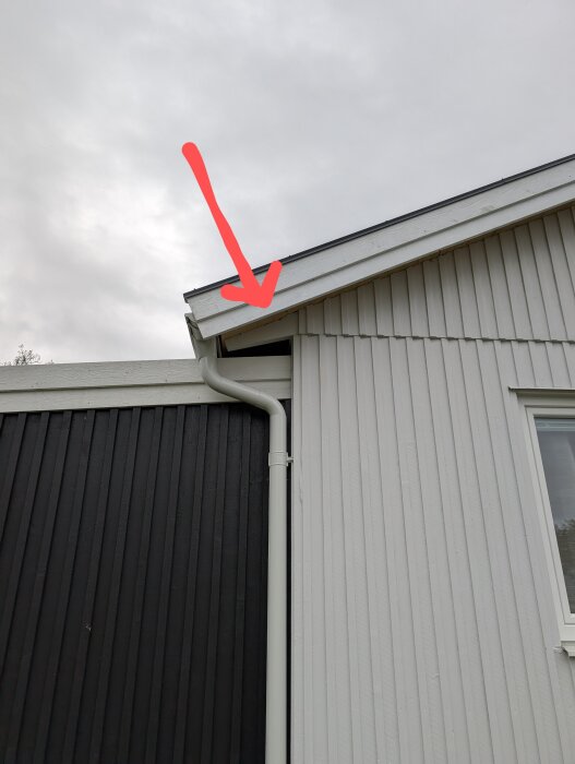Pilen pekar på takfoten över uterummet där råsponten är bytt. Bilden visar en trång plats vid hängrännan där det är svårt att måla brädorna.