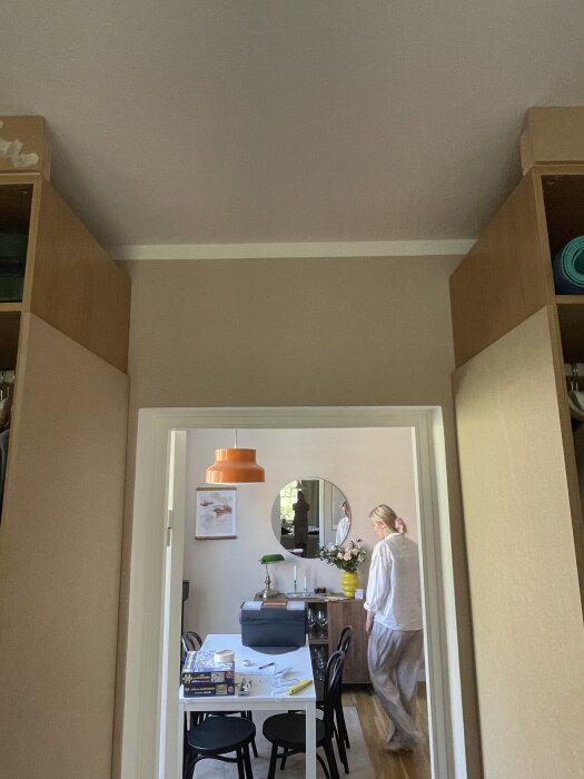 Vägghängd placering ovan dörröppning med synliga garderober i beige färg, person går i bakgrunden.