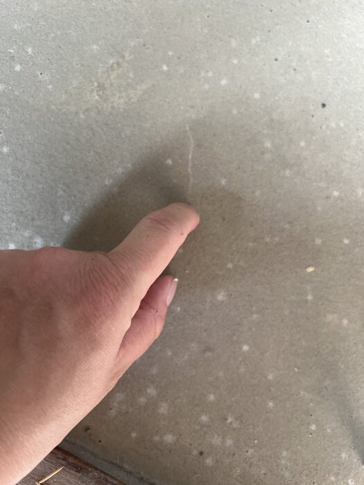 Hand som trycker på nylagt, ännu inte helt härdat flytspackel i en hall, som ser fuktigt ut.