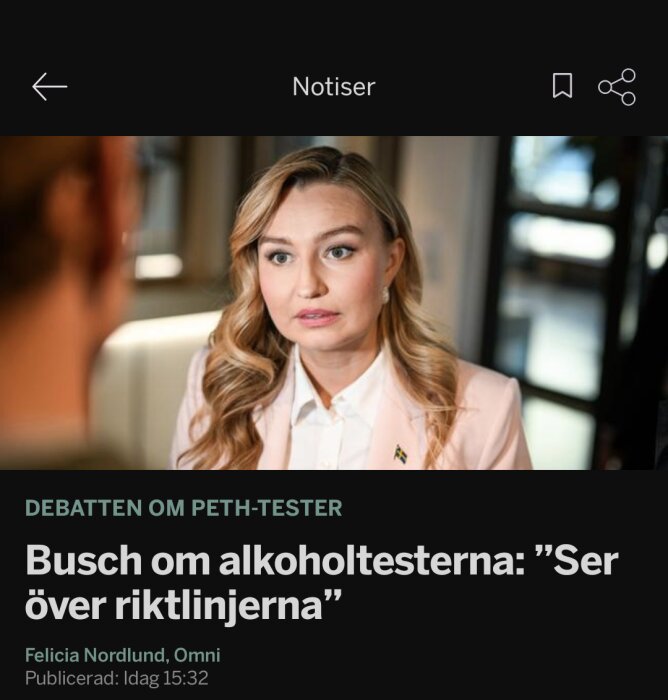 En person med blondt hår pratar med någon i en inomhusmiljö, iklädd kavaj, i en diskussion om alkoholtesternas riktlinjer.