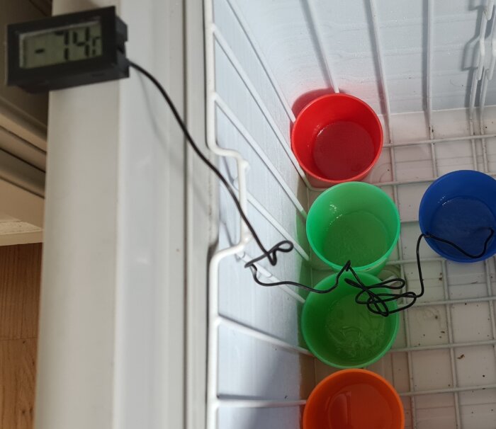 Plastglas med vätskeblandningar i en frys, termometern visar -7,4°C, färgglada glas.