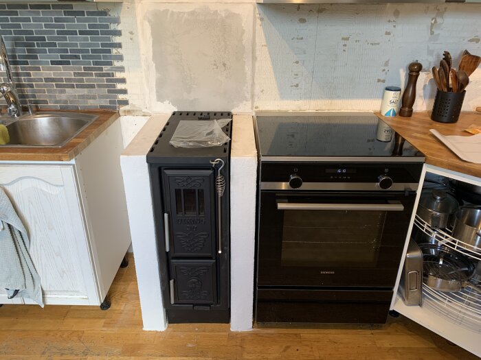 Vedspis och ugn i kök, med murade väggar och kakel, visar renoveringsframsteg i köket.