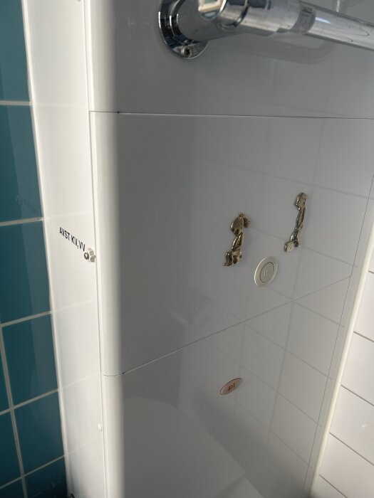 Vit skåpsenhet i badrum med texten "AVST KV, VV" synlig på sidan och två mässingsfärgade vred samt en rund knapp framtill.
