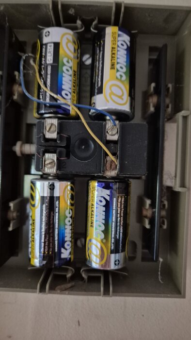 Bilden visar ett batterifack med fyra Konnoc super alkaline-batterier och anslutna kablar, som används för att illustrera ledningsplacering.