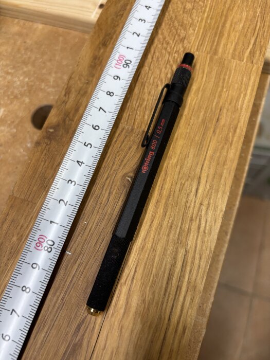 Svart Rotring 800 0,5 mm stiftpenna och en rullande måttstock på ett träbord.
