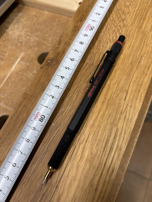 Svart avancerad penna och måttband på träytan av arbetsbänken.