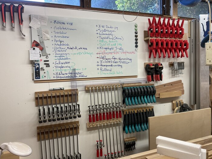 Verkstadsvägg med flertalet verktyg och klämmor organiserade, samt en whiteboard med anteckningar och ritningar.