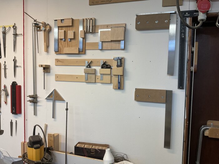 Verkstadsvägg med verktygsförvaring, inklusive stora vinklar, snickarverktyg och en whiteboard. Diverse verktyg och material syns på arbetsytan.