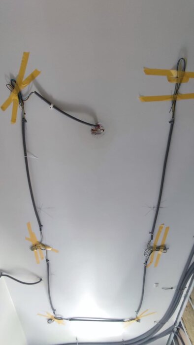 Elektriska kablar fastsatta i tak med gul tejp under badrumsrenovering i lägenhet från 1970.