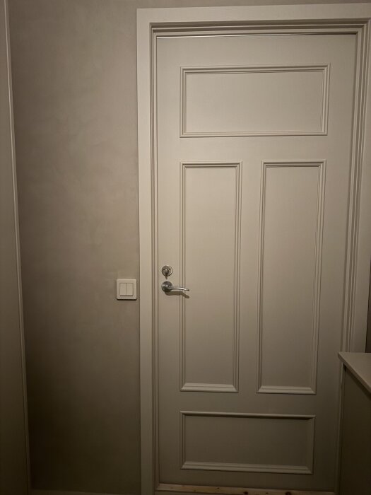 En stängd dörr med en vit strömbrytare på väggen bredvid, diskussion om att byta plats på funktionerna bakom strömbrytarknapparna.