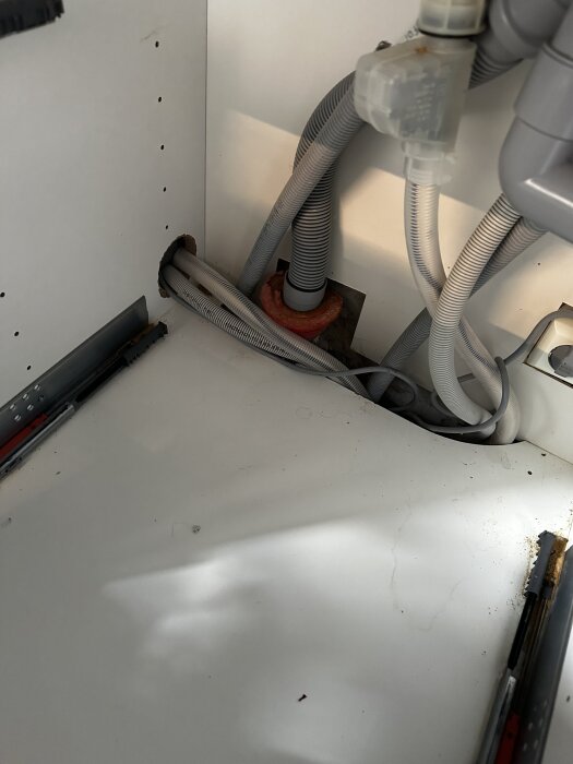 Avloppsrör och slangar under köksskåp i en krypgrund, med rörgenomföring genom väggen och bjälklag synligt.