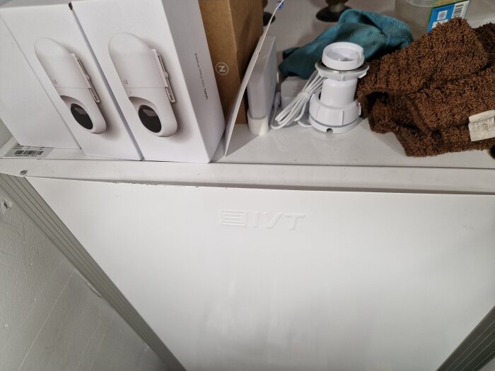 Fronten på en IVT varmvattenberedare omgiven av kartonger och textilier ovanpå, i en byggnad eller renoveringsmiljö.