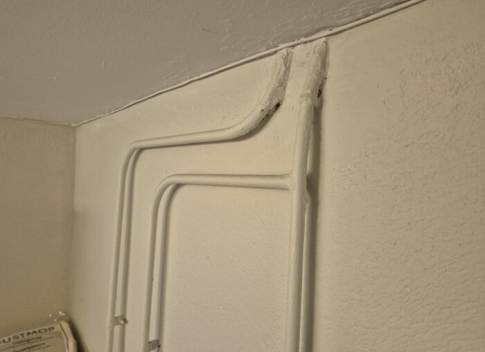 Ledningar sticker ut från väggen nära taket i en källartvättstuga, vilket kan utgöra en utmaning för renovering och kakelsättning.