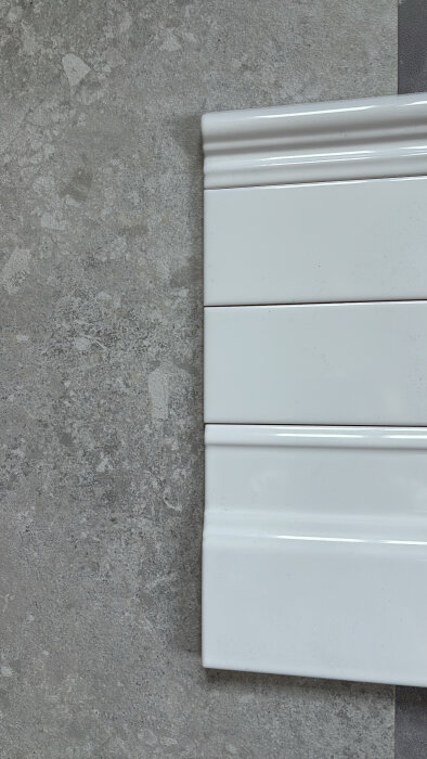 Vitt kakel mot grått stengolv, del av badrumsrenovering.