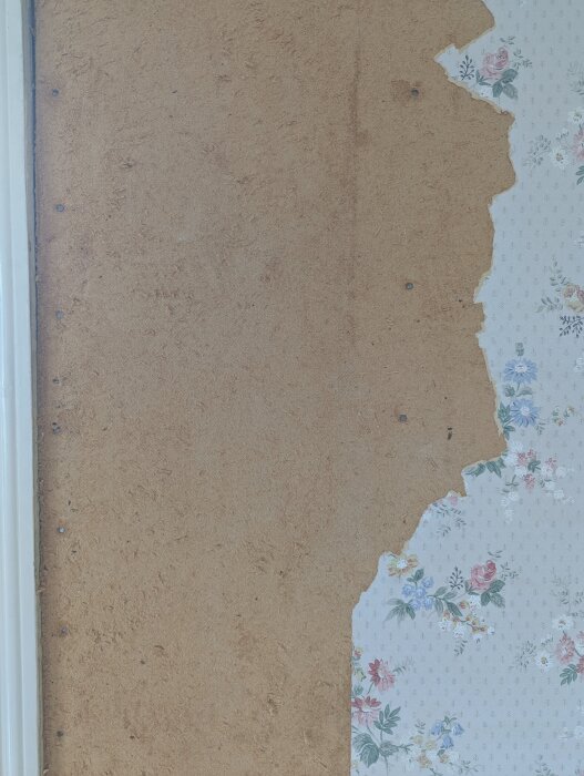 Halvavskalad tapet med blommönster visar bakomliggande trävägg.