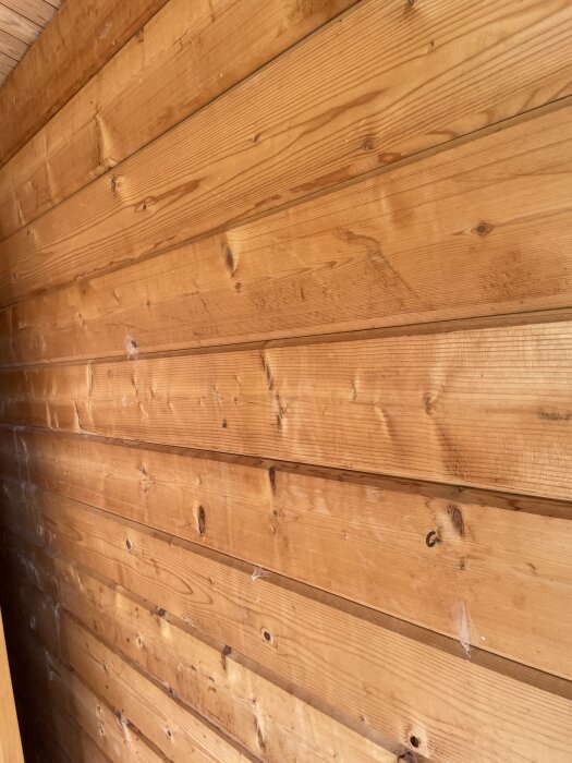 Inre vägg i friggebod med träpanel och mellanrum mellan brädorna, potentiellt för luftspalt vid isolering.