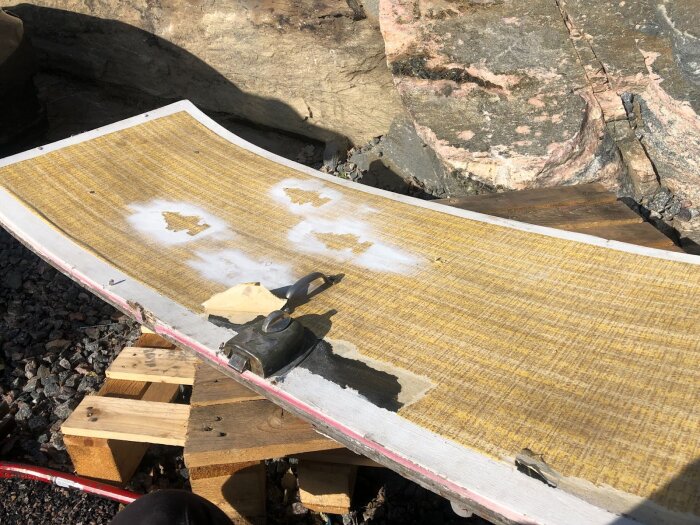 Tunn plåt redo för bearbetning på provisorisk arbetsyta, inramad av träklossar, med verktyg och materialrester ovanpå.