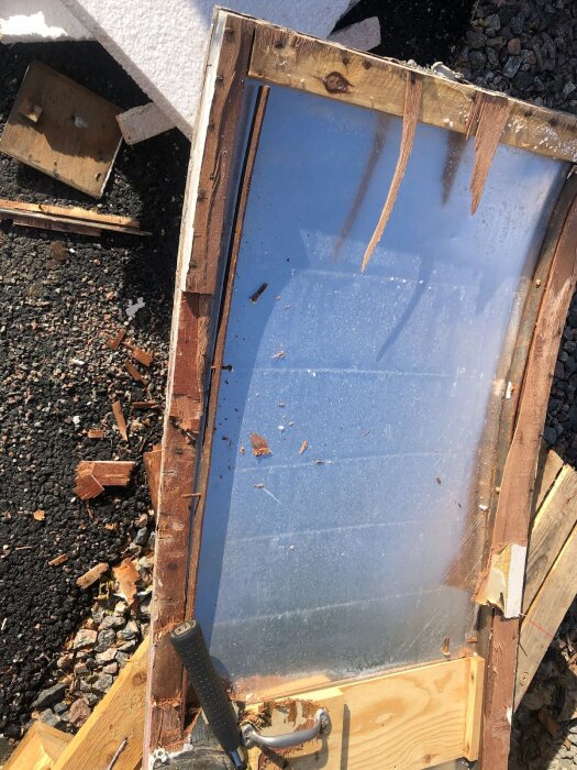 Gammal dörrstomme med borttagen beklädnad, exponerad trä- och aluminiumstruktur, omgiven av diverse byggmaterial på marken.