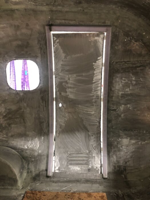 Nybyggd dörr i aluminium under dörrbygge, med plåt insatt i dörröppning, tejpad för att hålla form, omgiven av grå väggar.