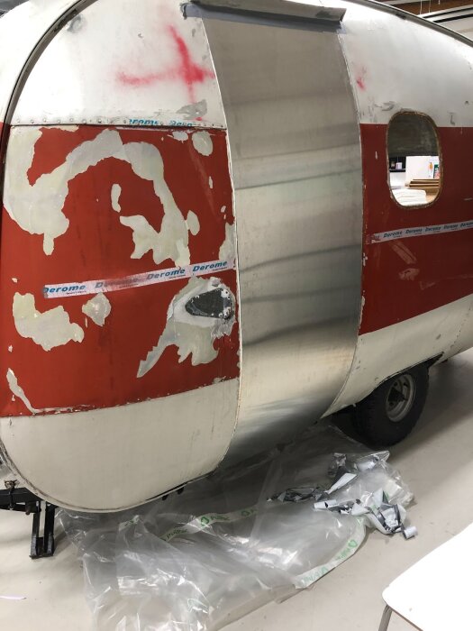 Halvfärdigt dörrbyte på en husvagn med borttagen panel och framträdande nytt metallskikt under återuppbyggnad, omgiven av plastskynken.
