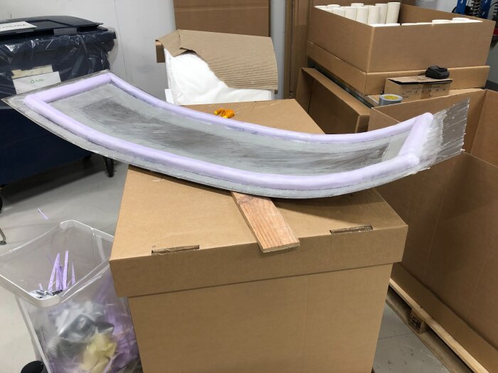Aluminiumplåt böjd för dörrbygge ligger på kartong, förstärkt med rosa XPS-balkar. Verktyg och kartonger i bakgrunden.