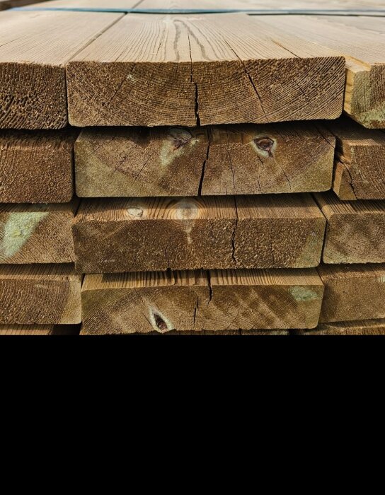 Staplat trävirke med sprickor och färgvariationer, markerat som premiumkvalitet för altanbygge.