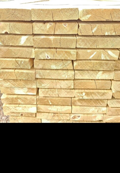 Staplat virke med sprickor och ojämnheter, köpt för altanbygge. Detaljer om kvaliteten på det "premium" levererade virket ifrågasätts.