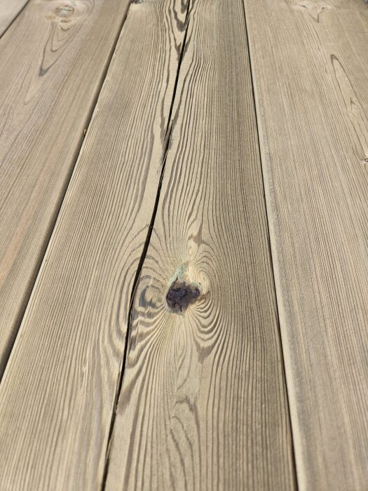 Träplankor med synlig kvist och sprickor nära centrum, del av ett premium virkesparti för altanbygge.