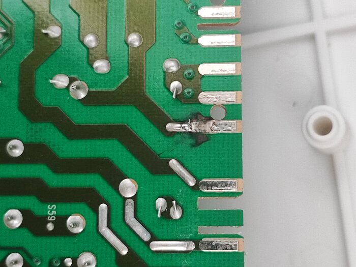 Närbild av kretskort med möjligt skadat område och brända fläckar. Banor och lödpunkter synliga på grön yta.