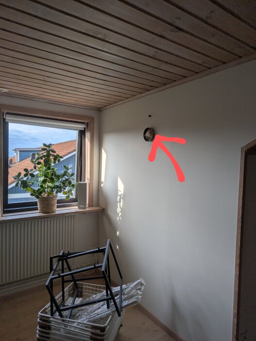 Vägg med ett litet runt hål för ventilation eller AC-installation, bredvid ett fönster med en krukväxt.