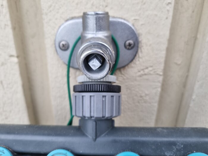 Utedel av tappkran utan märke monterad på vägg, med en knottrig koppling och del av grön slang synlig i bakgrunden.