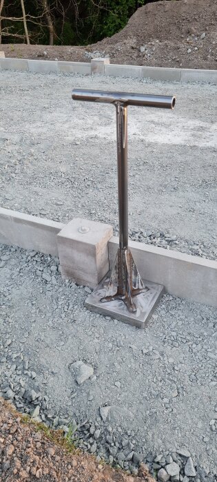 Handstamp i metall på grus underlag med några träd i bakgrunden.