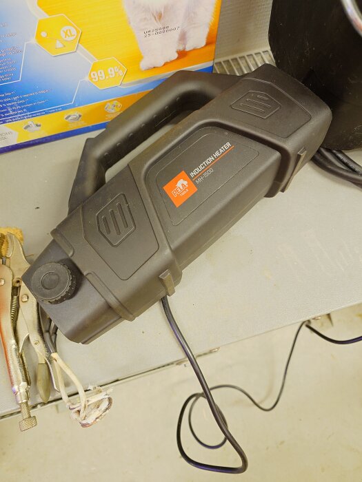 Induktionsvärmare med svart handtag ligger på ett bord, används för att reparera bromsar på a-traktor enligt inlägget.