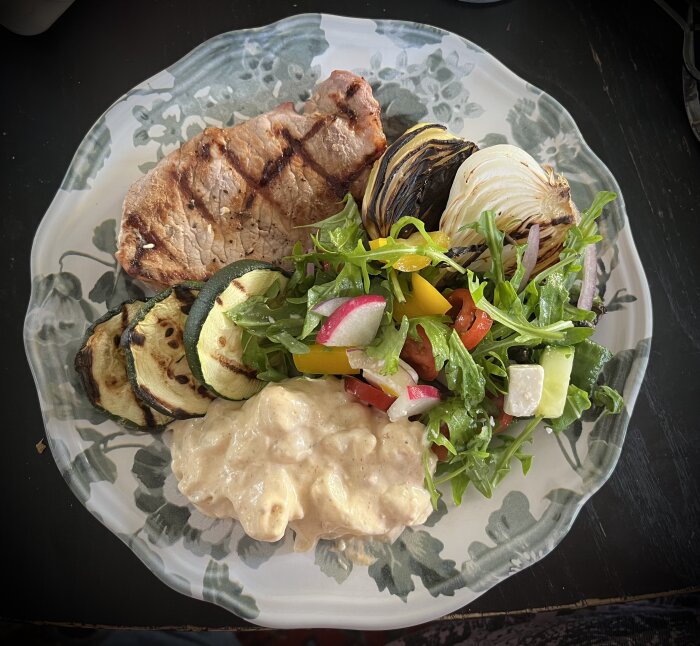 Grillade fläskkotletter, padrones, lök, squash på tallrik med potatissallad och grönsallad.