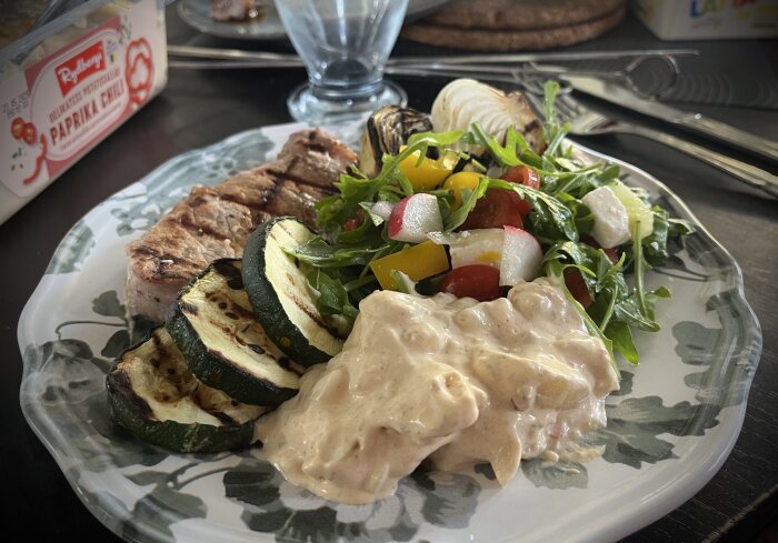 Grillad fläskkotlett med grillade zucchiniskivor, sallad och potatissallad med chili och paprika på en tallrik.