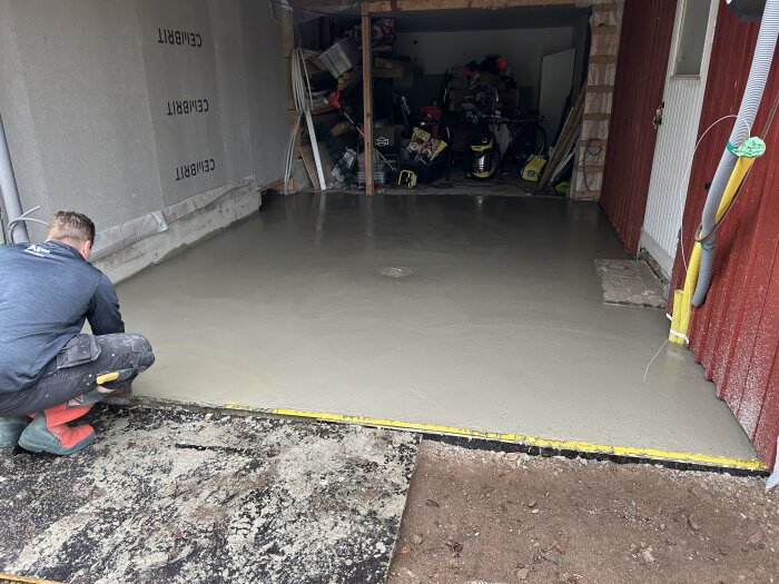 Man jämnar ut en nylagd betongplatta i ett garage, med betongstänk synligt på väggarna.