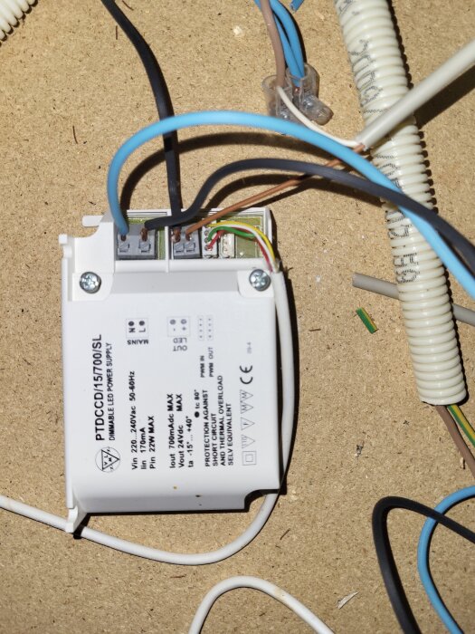 Dimbart LED-drivdon med anslutna kablar ligger på en trätavla. Text på drivdonet specificerar tekniska detaljer och märken.