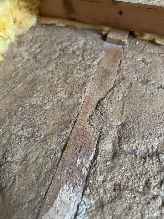 Brun betongplatta med trärester och isolering synliga, en del av husets grundkonstruktion från ett rivet golv i ett rum från ett 1973 byggt hus.
