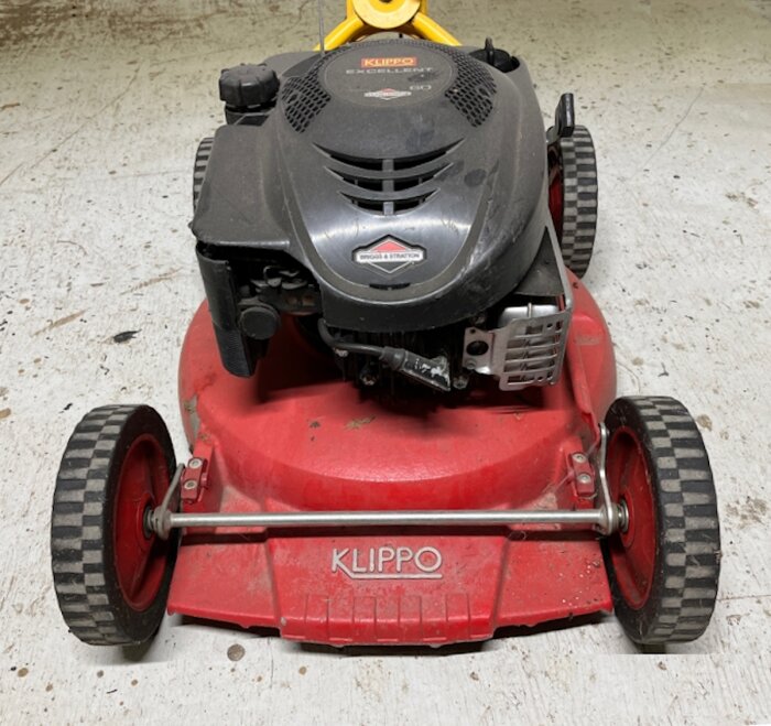 Klippo gräsklippare med Briggs & Strattonmotor på röd kropp, stående på en betongyta.