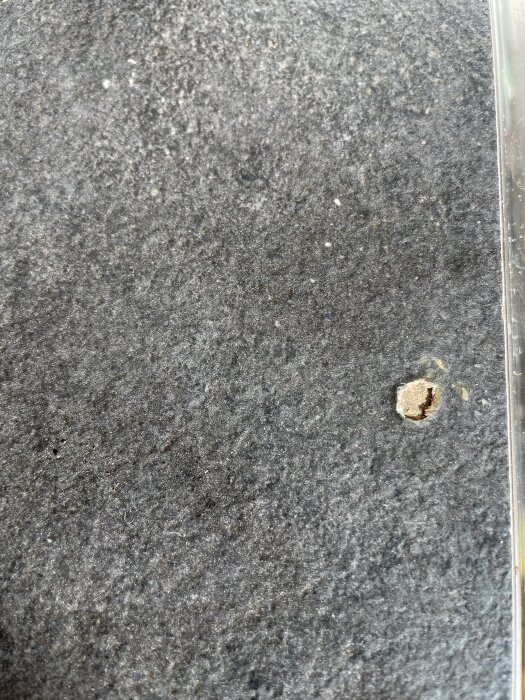 Närbild på en sliten mörk yta med en liten skada eller hål på ena sidan.