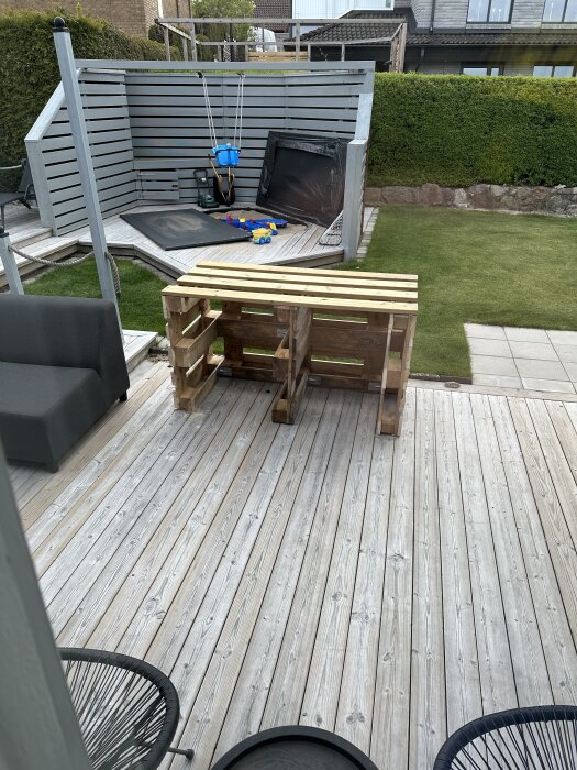 Pallar på en trätrall med leksaker i bakgrunden, planerad för att bära en granitskiva. Trädgård och lekplats syns också.