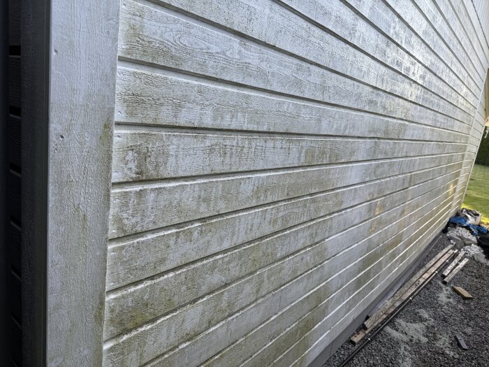 Smutsig garagefasad före tvätt, träpanel med gröna alger och smutsfläckar.