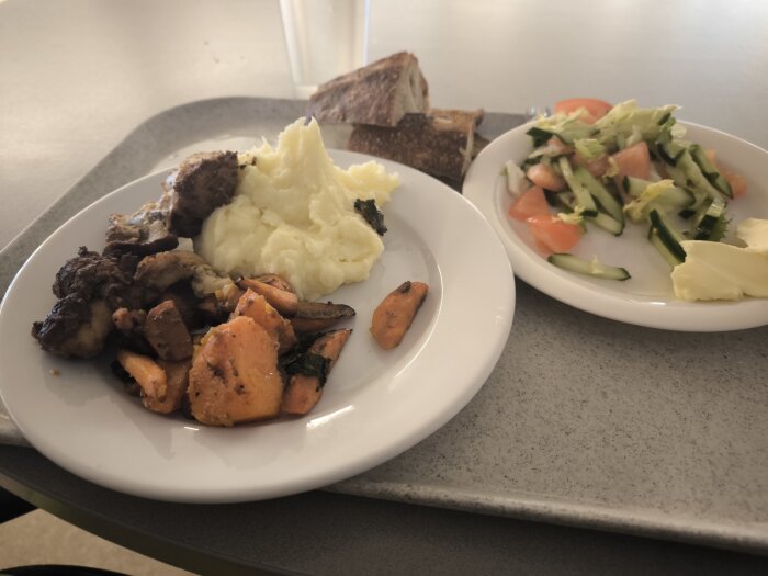 Tallrik med kyckling och potatismos, serverad med sallad, bröd och smör på en bricka.